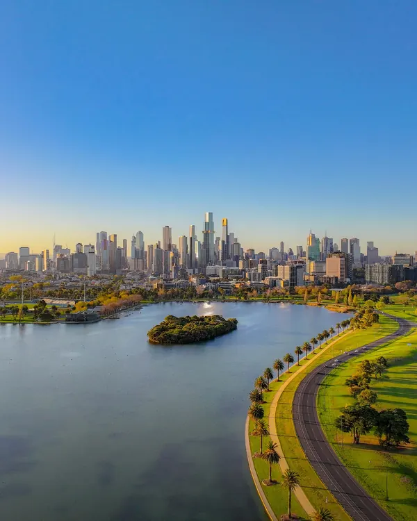 Aerial view of Albert Park Lake at sunset with Melbourne skyline reflecting golden light