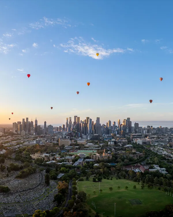 Hot air balloons floating over Melbourne CBD at sunrise, photographed from a drone at altitude