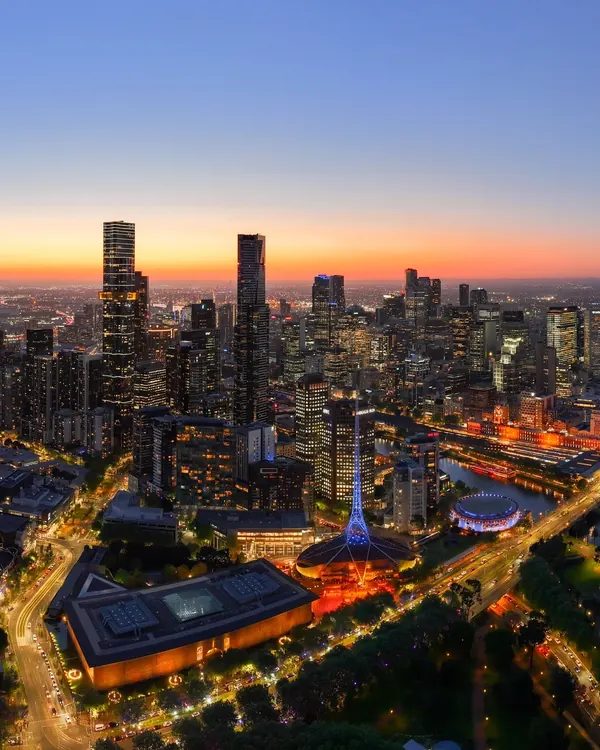 Aerial view of the Melbourne CBD skyline at twilight, tower lights glowing against a deep blue dusk sky