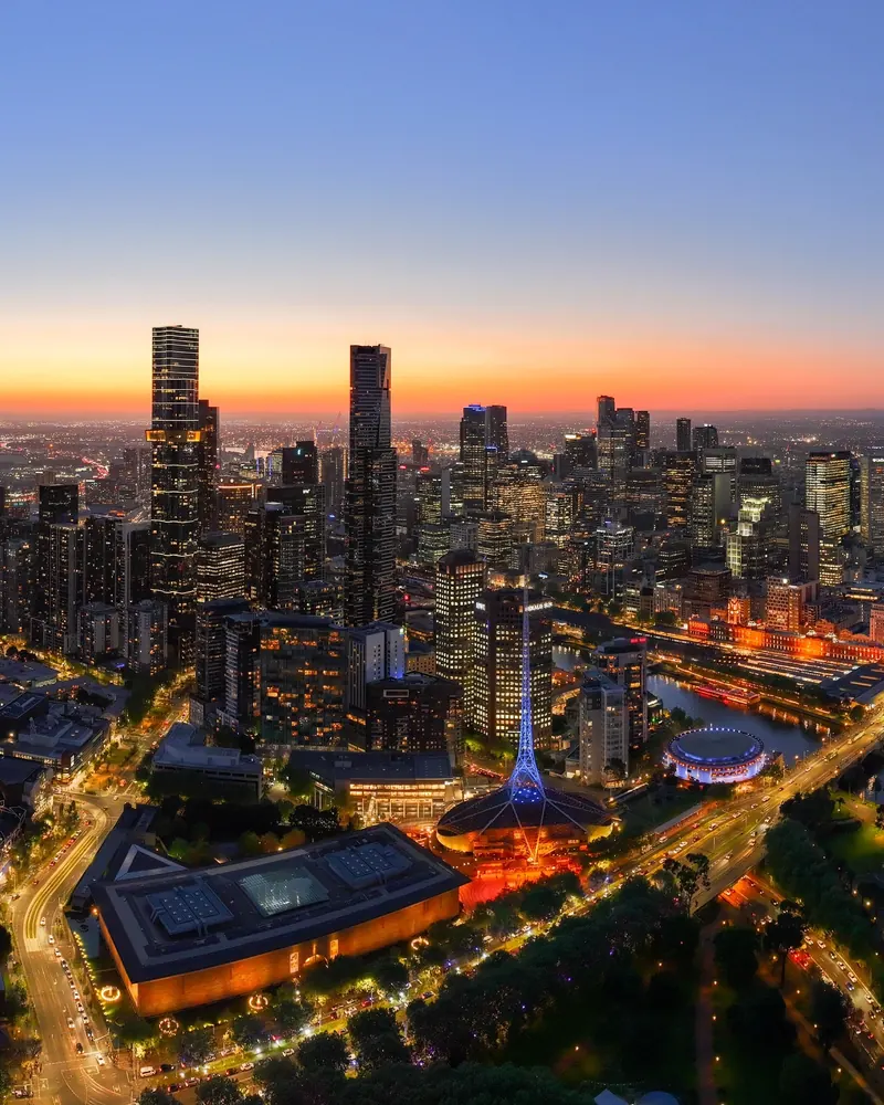 Aerial view of the Melbourne CBD skyline at twilight, tower lights glowing against a deep blue dusk sky